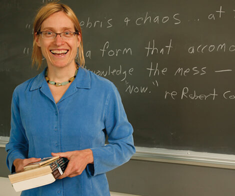 Photo of Nona Caspers holding books while standing in front of a chalkboard