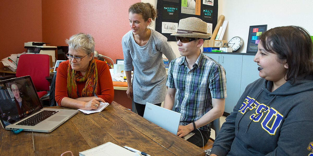Photo of four people looking at a laptop computer