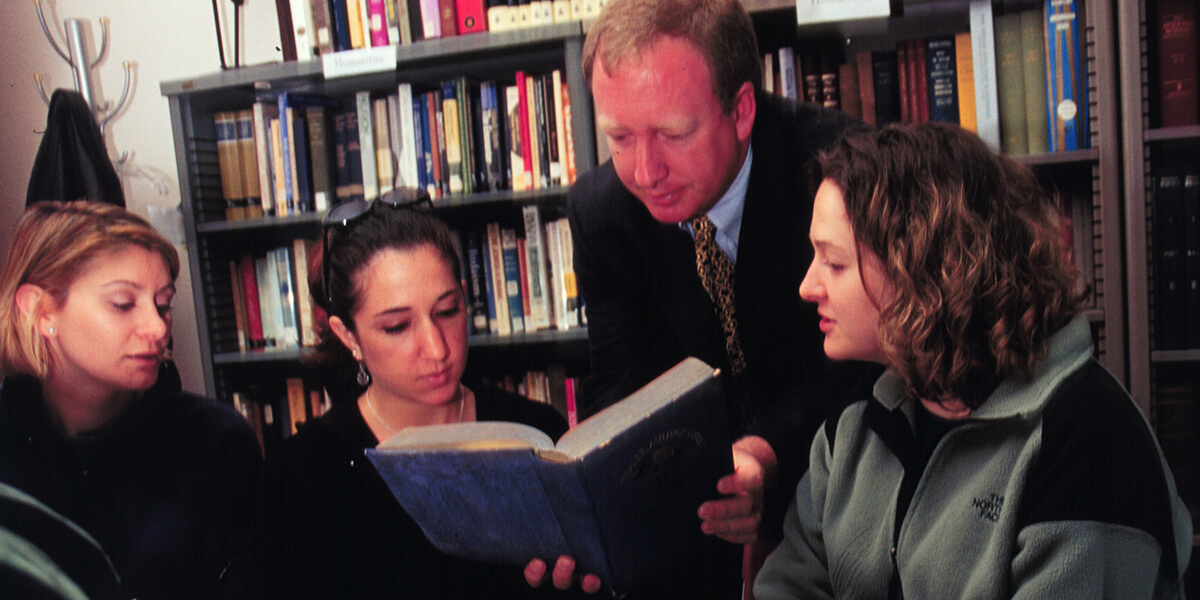 Photo of Marc Dollinger sharing a book with three students