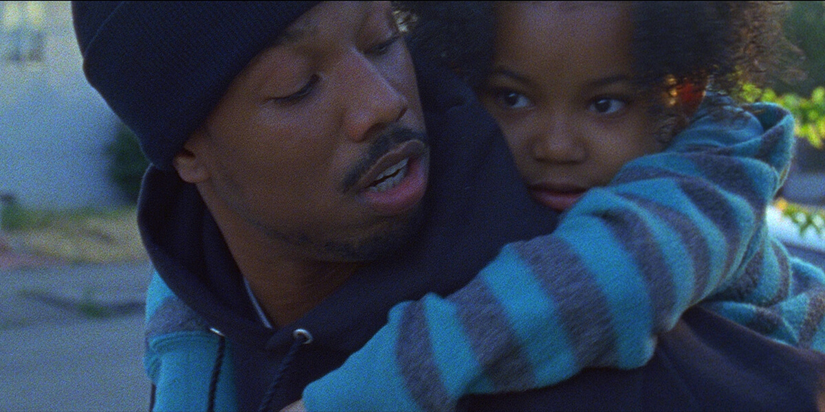 Still from Fruitvale Station of Michael B. Jordan as Oscar Grant carrying his daughter on his shoulder while looking back at her