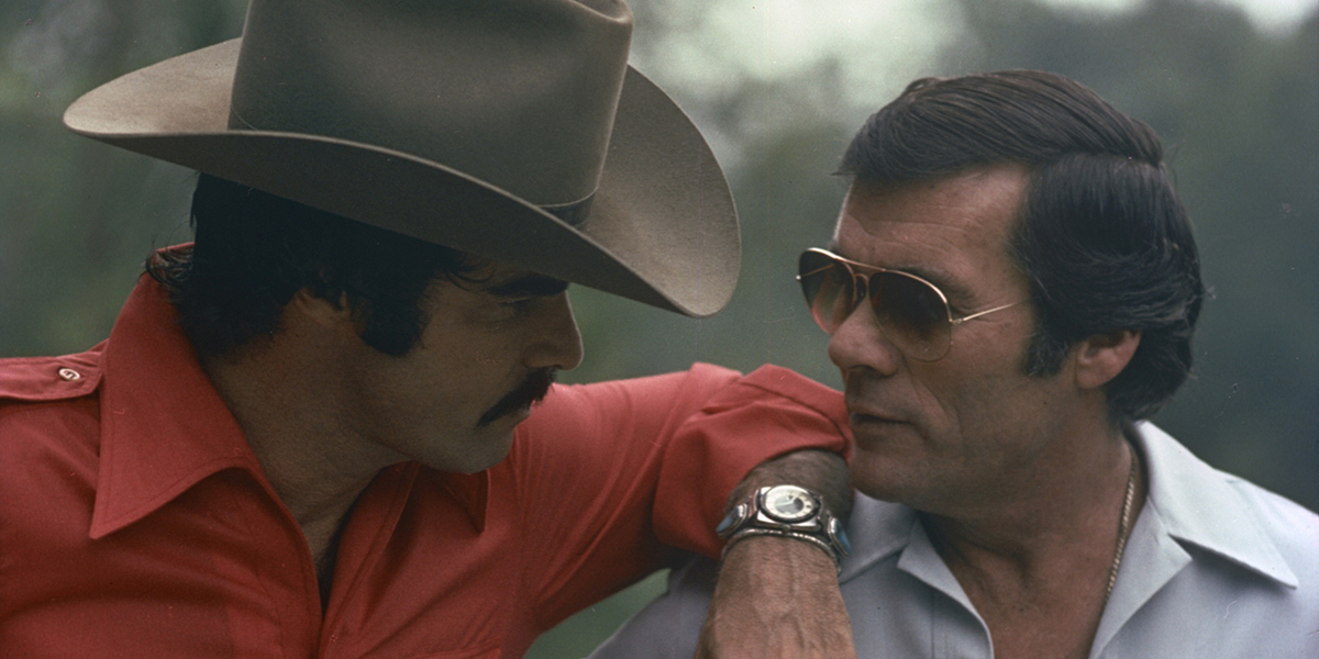 Photo of Burt Reynolds resting his arm on Hal Needham's shoulder