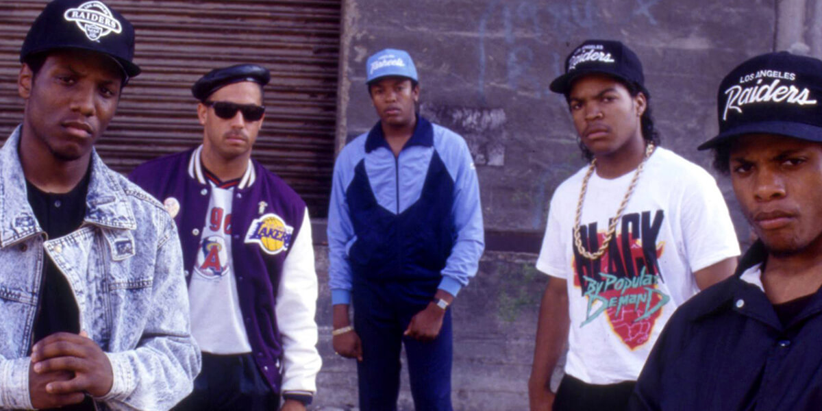 Photo of five members of N.W.A. standing in front of an industrial building