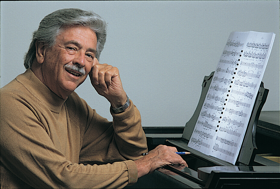 Wayne Peterson sitting at a piano with sheet music and holding a pencil in his left hand