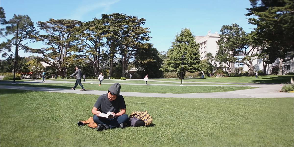 Photo of student Roger Habon sitting on the grass and reading