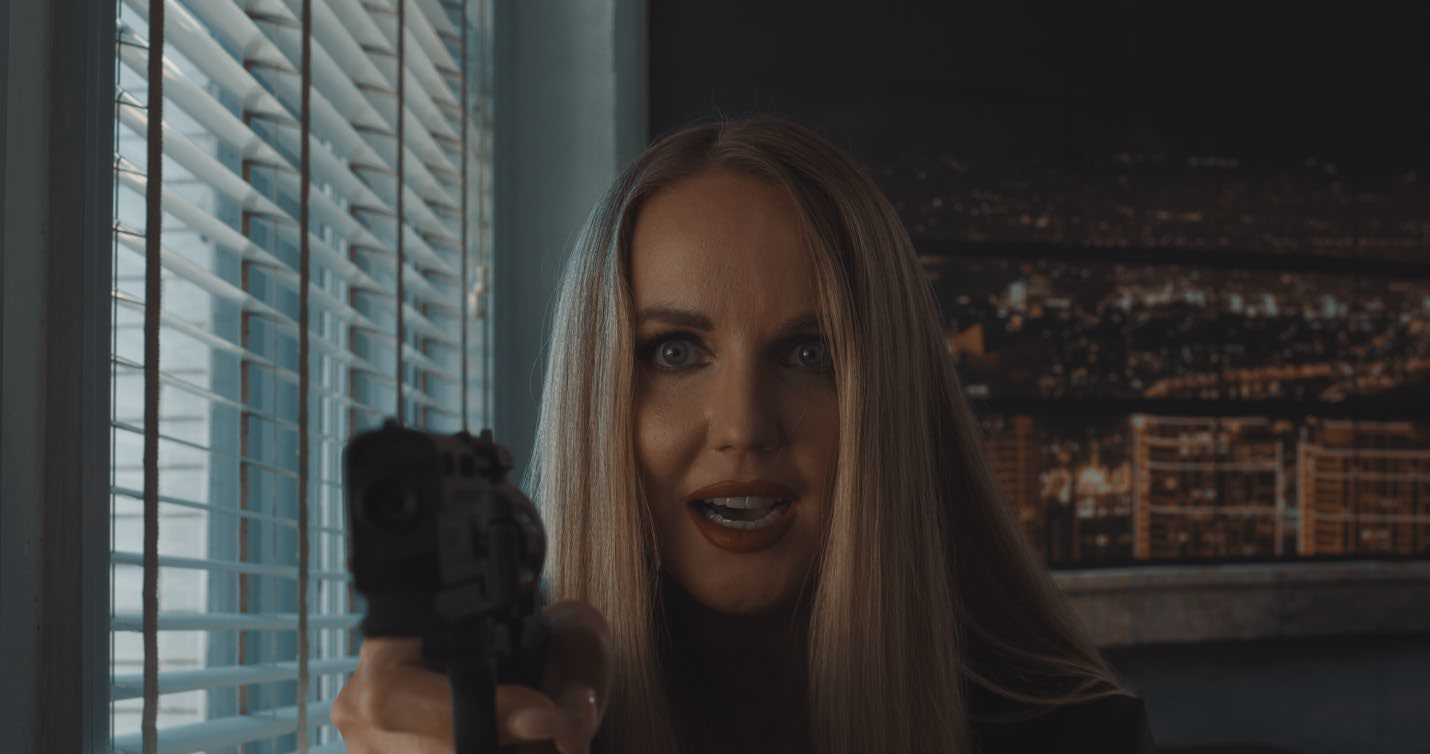 Blonde woman pointing a gun at the camera