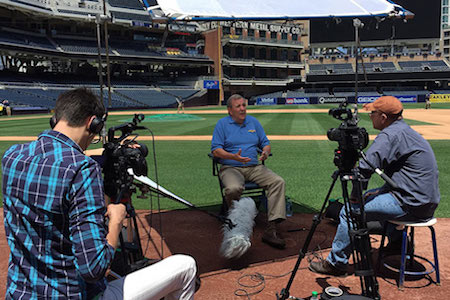 Camera crew interviewing man on baseball field