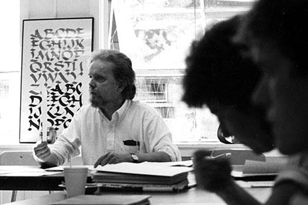 Man seated and speaking with silohuette of person's head in the foreground