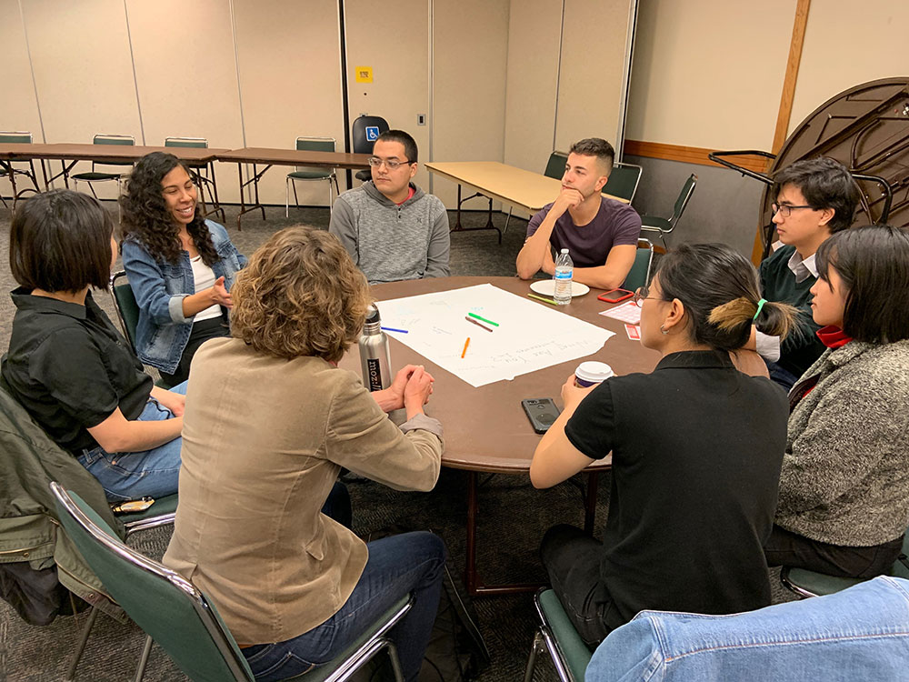 Eight students gathered around table in discussion