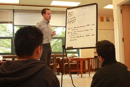 Instuctor referencing whiteboard with writing, student in foreground