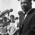 The Rev. Martin Luther King Jr. speaks in front of a podium with about 10 microphones attached to it