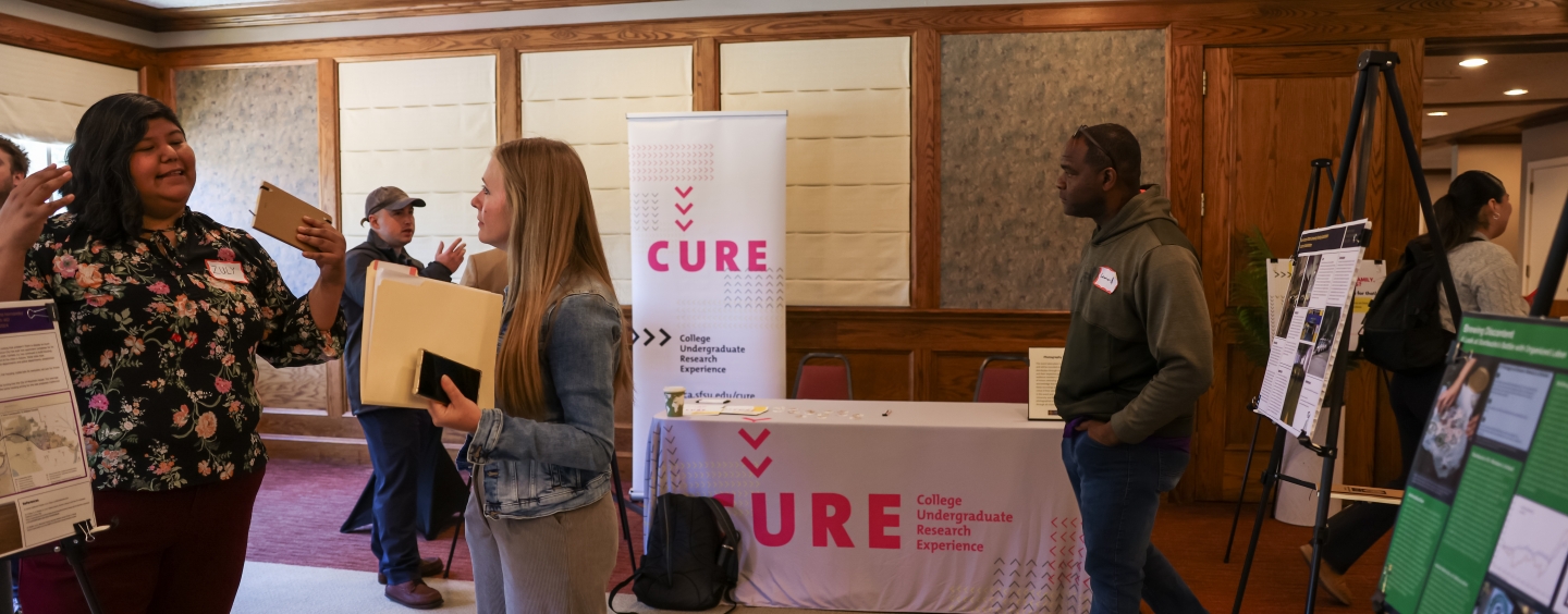 Visitors looking at posters with a table for CURE in the back