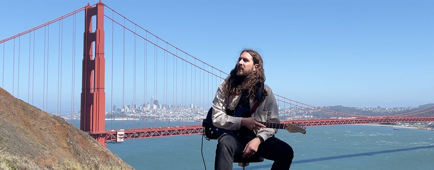 Nate Mercereau seated outdoors in the Marin Headlands holding a guitar