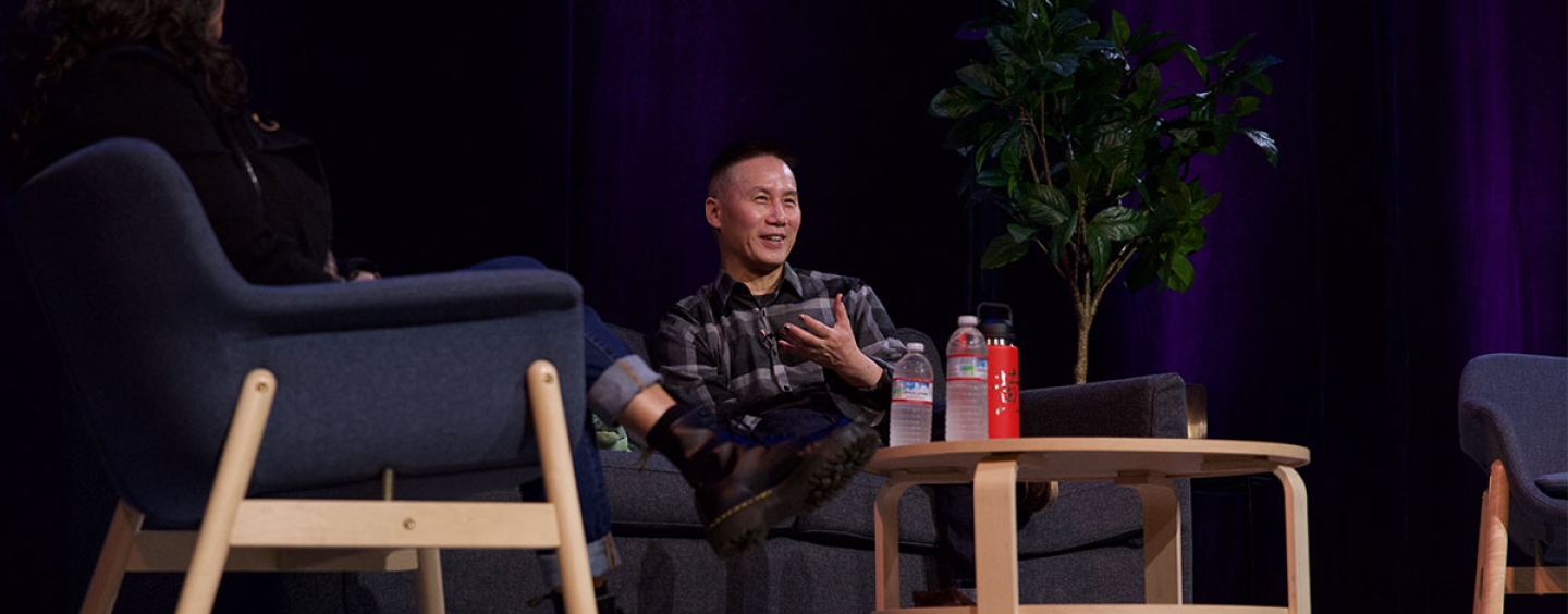 Actor BD Wong sits in a chair on a stage across from a woman