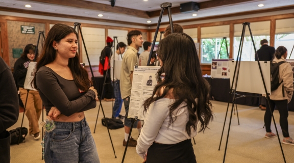 Two students talking in front of a project on an easel.